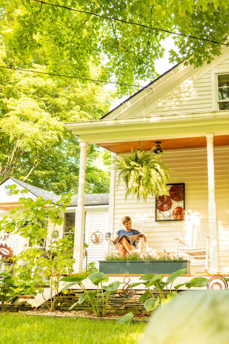 Woman sitting on a rocking chair on her front porch reading the newspaper.