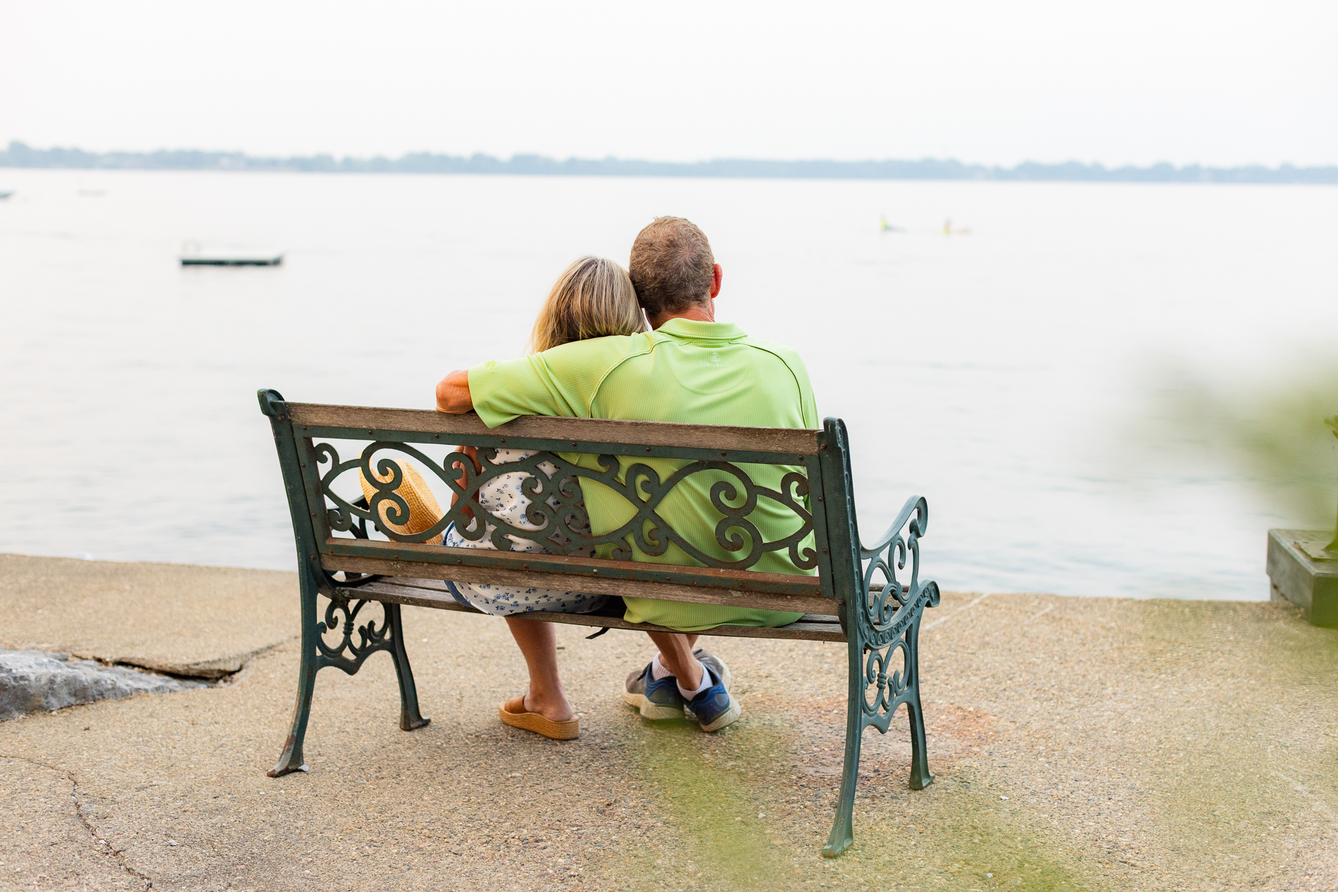 Older couple sits close together on a bench overlooking a calm lake, suggesting peace, connection, and a relaxed retirement.