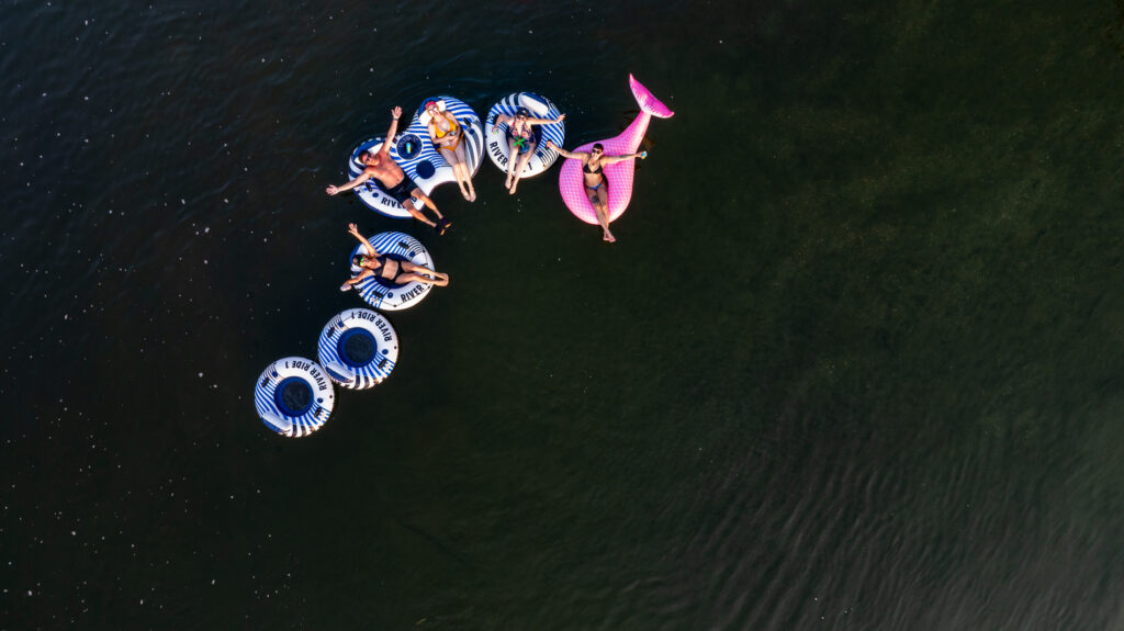 Aerial view of a group of people relaxing on inflatable tubes and a pink float in a calm, dark green river.