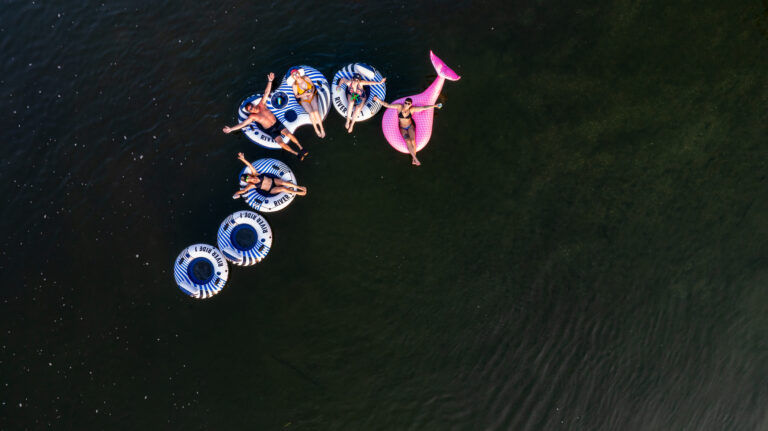 Aerial view of a group of people relaxing on inflatable tubes and a pink float in a calm, dark green river.